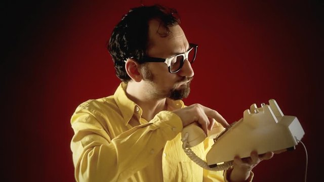 A funny ugly nerdy man dialing a number and happily chatting on a vintage retro rotary phone.
