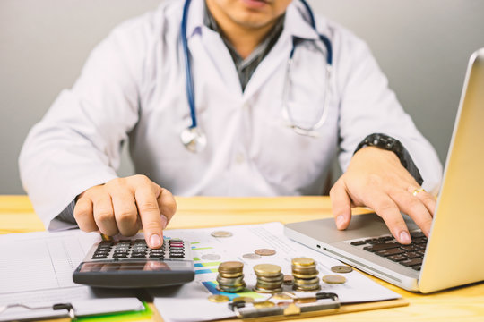 young medical doctor caucasian healthcare professional wearing a white coat with stethoscope in hospital ,calculates on an electronic calculator,medical fee concept,selective focus,vintage color