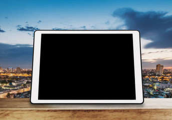 Digital tablet, isolated black screen on wooden table with blur city skyline background
