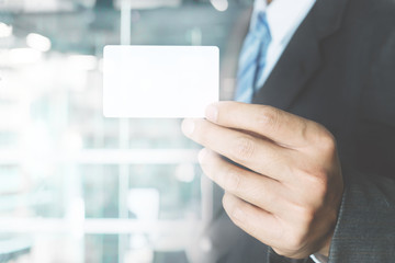 Young business man wear suit holding white business card on modern office blur background.