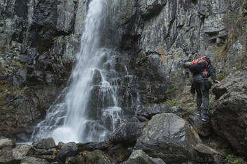 A backpacker with a backpack and a Mat makes his way to the waterfall among the rocks