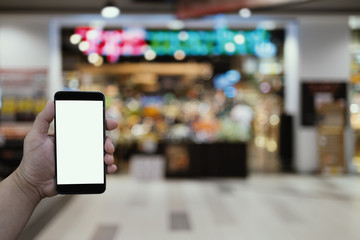 blank screen smart phone in hand with blurred background of shopping mall, digital life; internet of things concept