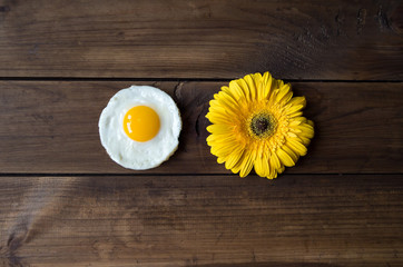 Obraz na płótnie Canvas round shaped fried egg with yellow gerbera on dark wooden backgrond