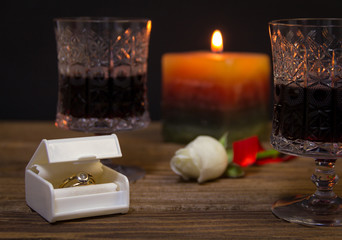 Obraz na płótnie Canvas Engagement ring on the table with wine, a candle and a rose
