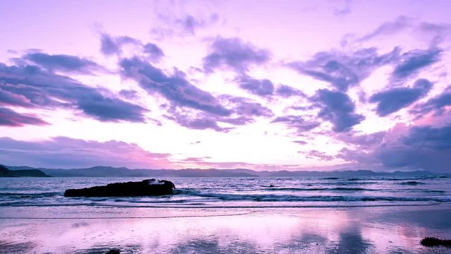Time lapse of a cloudy sky paint in pink by the last rays of the sunset above the sea and the mountain range of the Coromendel in the north island of New Zealand