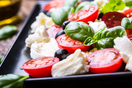Caprese Salad.Mediterranean salad. Mozzarella cherry tomatoes basil and olive oil on old oak table. Italian cuisine.