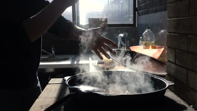 Hands of the cook prepare pilaf in cauldron