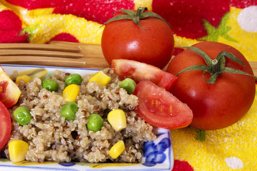 Quinoa salad with corn and green peas on plate with tomato