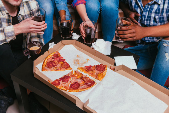 International home pizza party, interracial friendship. Four unrecognizable friends have fun leisure with unhealthy food and drinks, top view.