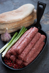 Frying pan with raw cevapi or balkan traditional skinless sausages, onion, garlic and pita bread