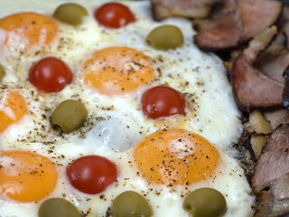 fried eggs with bacon, olives and tomatoes a hearty breakfast. 