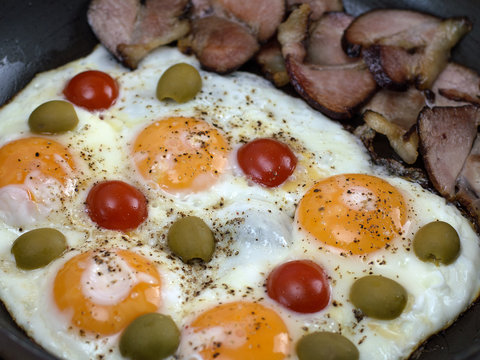 fried eggs with bacon, olives and tomatoes a hearty breakfast. 