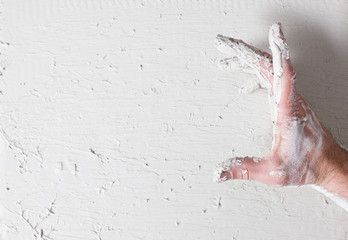 Dirty worker hand in stucco hold something on white plaster wall. Building background for advertisement or commercial. Free space.
