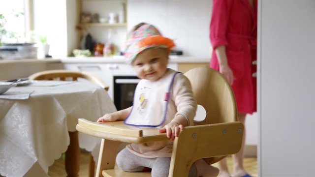 Little baby girl sitting in baby chair and clapping tiny hands in rhythm of music listening enjoying having fun and wearing  cute hat
