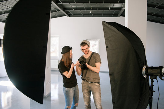 Model and photographer enjoy photos on camera. Man with camera show pictures to happy casual woman during the studio session.