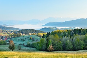 Fototapeta na wymiar Spring meadows and fields landscape in Slovakia. Low Tatras panorama with snowy peaks. Blooming cherry trees. Cloudly inversion after the rain.