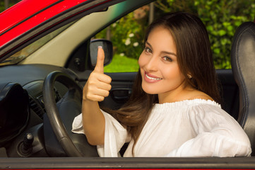 Fototapeta na wymiar Beautiful smiling girl in red car with thumbs up signal of victory
