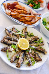 Freshly grilled sardines on a plate with lemon and fried potatoes