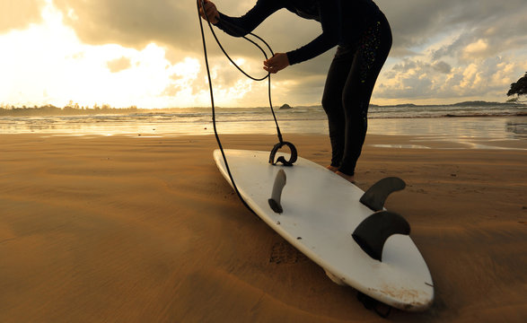 young woman surfer with ready to surf on a beach at sunrise