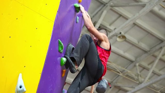 Muscular Climber Man Climbing Up On Color Rock Wall In Gym. Slow Motion Effect
