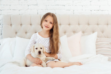 Girl sit on the bed with labrador puppy, indoor
