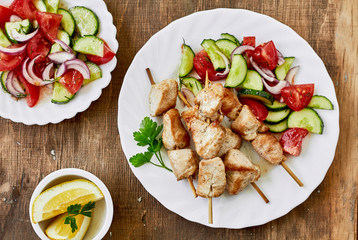 Chicken kebab and fresh vegetable salad on a wooden background, top view