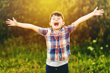 Happy kid boy of 6 year old having fun outdoors wearing blue plaid shirt, arms wide open
