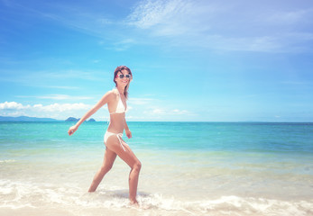Beautiful young woman in a white bikini walking along a tropical beach with azure water and white sand