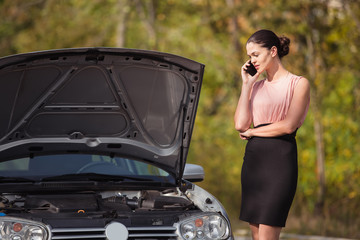 Young woman calling in evacuation service. Her car broke down on the road.