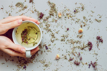 Tea background. Hands holding cup of hot tea. Dry herbal tea on the gray background, top view. Copy space