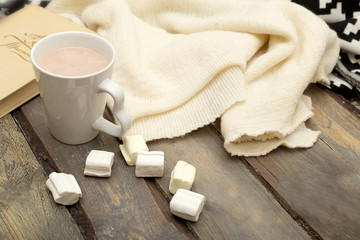 Cup of hot chocolate, marshmallow, book, candle on a wooden background.