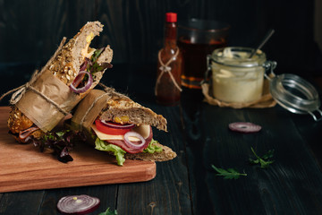 Fresh tasty submarine sandwich and sauces on the wooden dark table