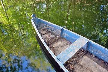 The front of an old wooden boat on the water reflecting the forest.