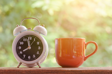 white alarm clock with red cup of coffee on wooden with natural background