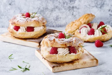 Gardinen Homemade choux pastry cake Paris Brest with raspberries, almond, sugar powder and rosemary, served on wooden serving board over gray blue texture background. French dessert © Natasha Breen