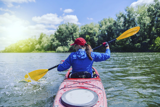 A girl rafts on a kayak on a river in a sunny day.