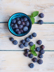 Fresh blueberries in blue bowl and leaves of mint on white wooden desk.