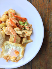 stir-fry vegetables with bean curd and shrimp in white dish with rice and fried egg on wooden background. Thai style Food.