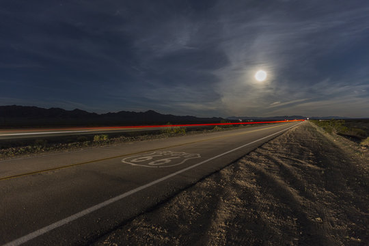 Route 66 sign with full moon and streaking train in the California Mojave desert.  