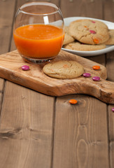 Fototapeta na wymiar Homebaked Chewable Butter Biscuits With Colored Chocolate Sweets. Carrot Juice. Olive Tree Board. Autumn Leaves.