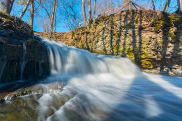 Waterfall in forest landscape long exposure flowing through trees and over rocks.