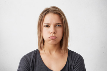 Studio portrait of young beautiful woman with dark eyes trendy hairdo wearing casual gray sweater blowing her lips being dissatisfied isolated over white background. People, lifestyle, emotions