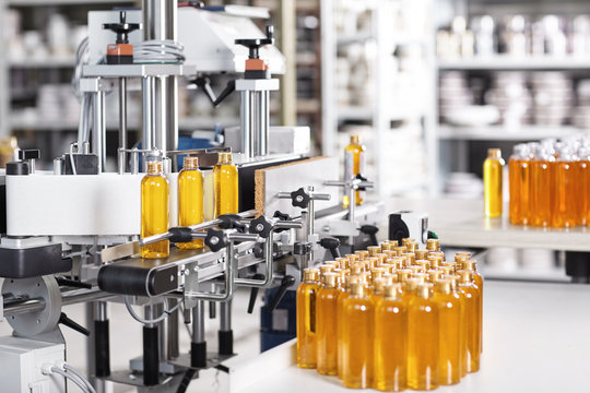 Bottles filled with soap yellow liquid standing on conveyor belt in factory. Automated process of creation soap on factory. Bottles with yellow thick substance standing in row going to be twisted