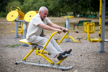 Obraz premium Old man making exercises on outdoor gym.