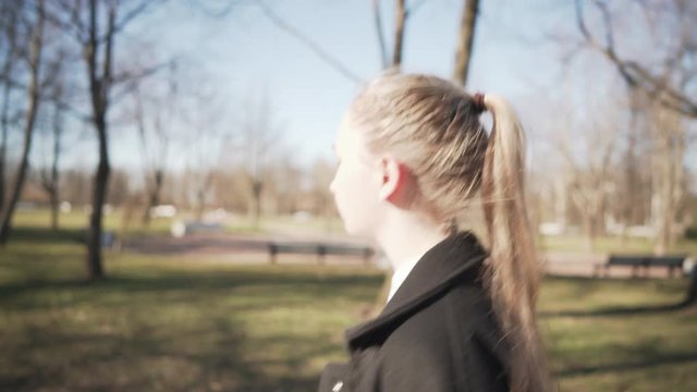 Gimbal low angle shot of female teen girl walking in town park in spring sunny day, uhd prores footage