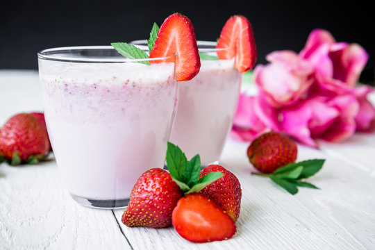 Strawberry smoothie with fresh berries and pink flowers on white wood table and dark background. Fresh milkshake