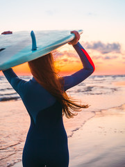 Surf girl with long hair with surfboard on a beach at sunset or sunrise and ocean