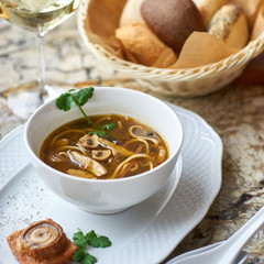 Asian cuisine. Mushroom soup with egg noodles served with toast, bread and white wine on marble background.