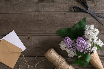 Lilac blossom on rustic wooden background with empty space for greeting message. Scissors, thread reel, small envelope. Top view