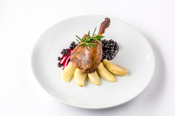 Duck leg baked with apples and currant sauce on white plate close-up view from above.